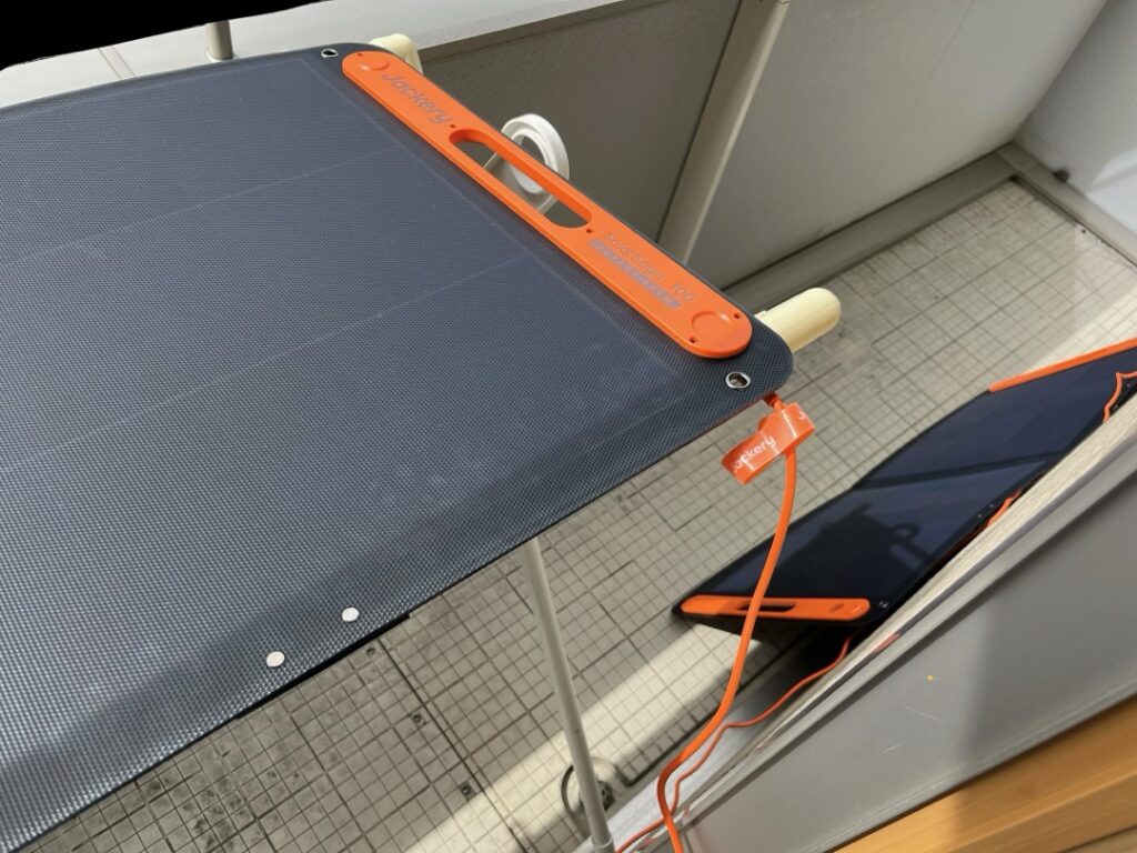 ベランダに設置された2枚のJackery SolarSaga 100。1枚は布団干し台の上に水平に近い角度で置かれ、もう1枚はベランダの床に直置きして壁面に立てかけられている様子。