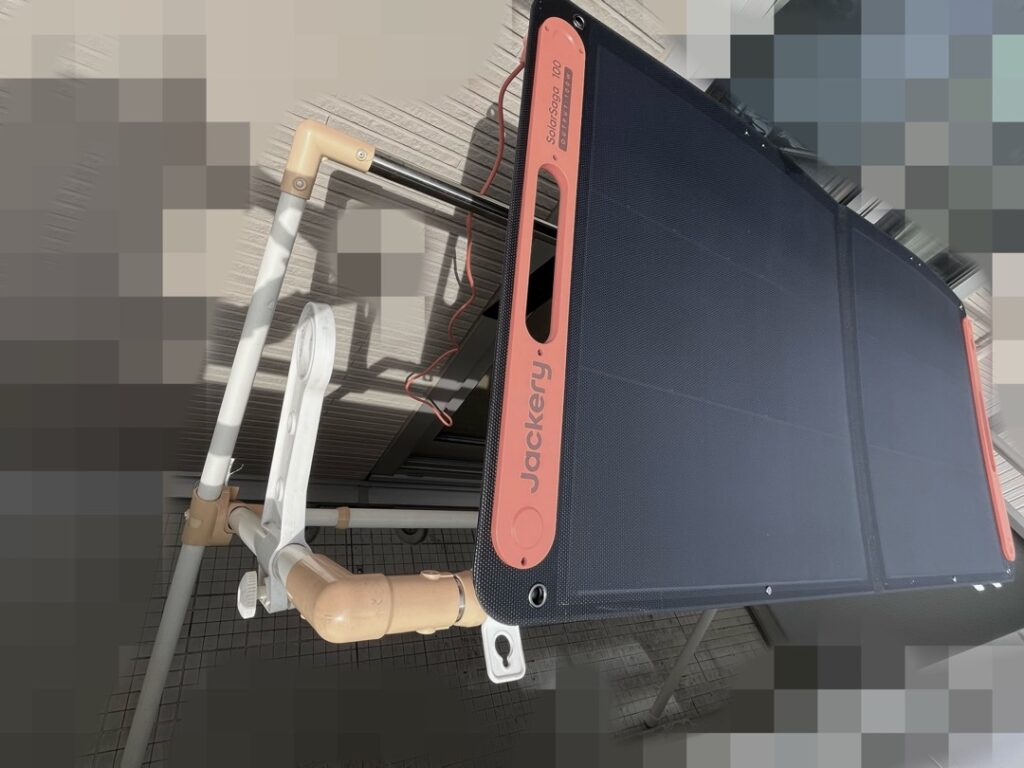 ベランダに設置された布団干し台の上にJackery SolarSaga 100Wソーラーパネルが固定され、直射日光で発電している様子の写真。